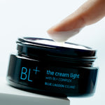 BL+ The Cream Light jar with cream being scooped by fingertip